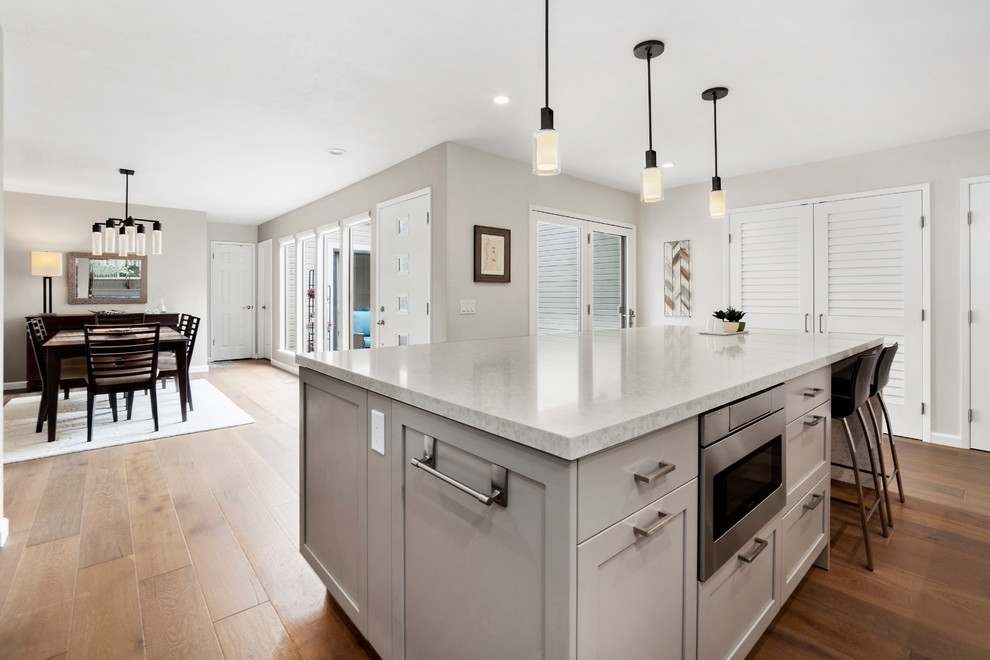Inspiration for a mid-sized transitional l-shaped medium tone wood floor and brown floor kitchen pantry remodel in Other with an undermount sink, shaker cabinets, white cabinets, quartz countertops, beige backsplash, subway tile backsplash, stainless steel appliances, an island and beige countertops
