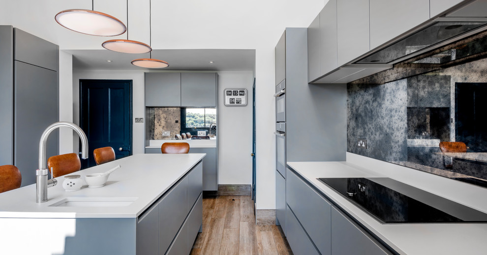 Idéer för ett mellanstort modernt kök, med en undermonterad diskho, släta luckor, grå skåp, flerfärgad stänkskydd, spegel som stänkskydd, svarta vitvaror, skiffergolv, en köksö och brunt golv
