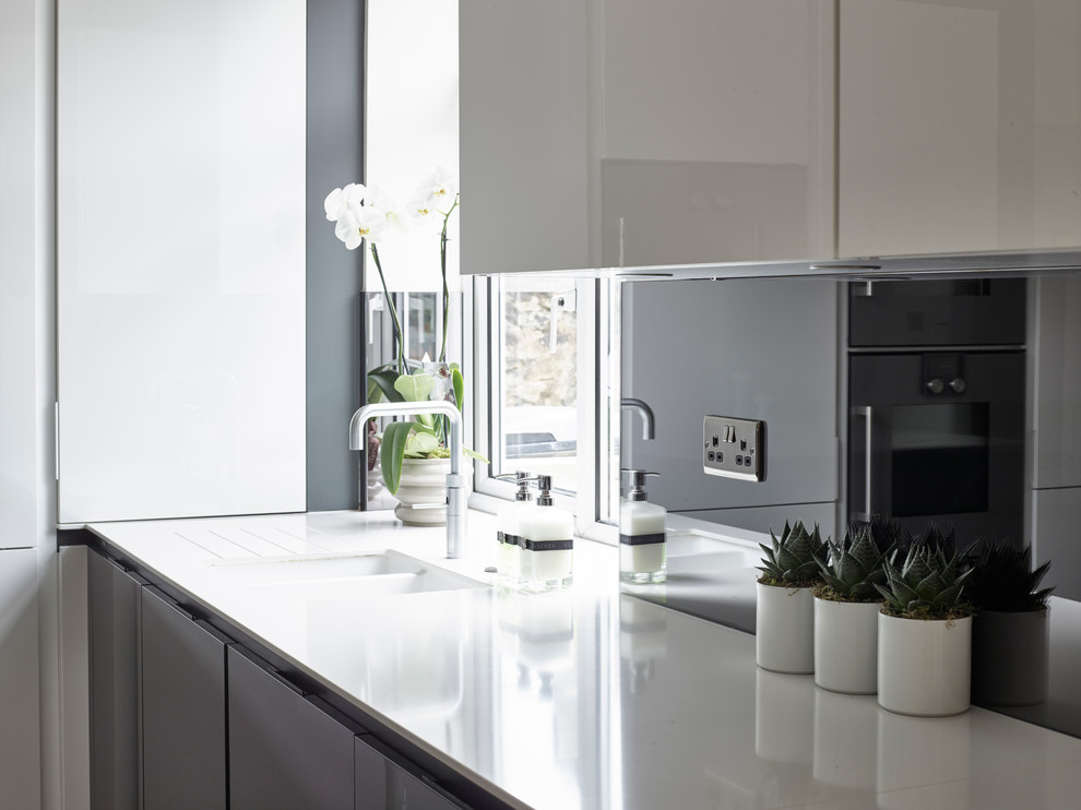 Large contemporary l-shaped open plan kitchen in Other with flat-panel cabinets, white cabinets, engineered stone countertops, grey splashback, mirror splashback, coloured appliances, porcelain flooring, an island, beige floors and white worktops.