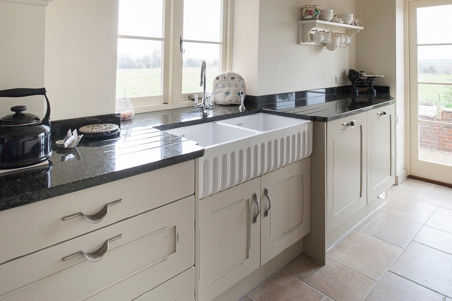 Small traditional galley kitchen in Kent with a belfast sink, white cabinets, granite worktops and porcelain flooring.