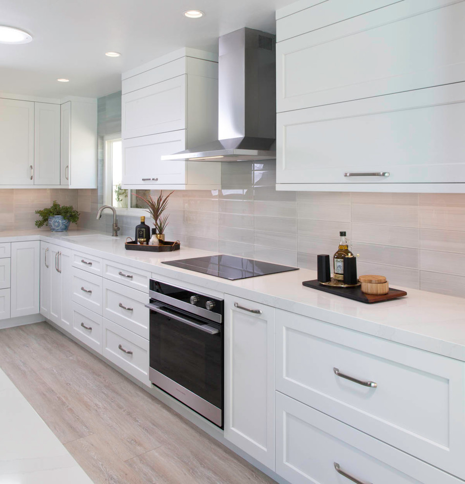 Photo of a large traditional l-shaped open plan kitchen in San Diego with a submerged sink, shaker cabinets, white cabinets, engineered stone countertops, grey splashback, ceramic splashback, integrated appliances, vinyl flooring, an island, beige floors and white worktops.