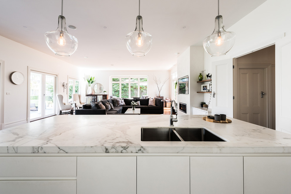 Medium sized contemporary single-wall open plan kitchen in Melbourne with a submerged sink, flat-panel cabinets, white cabinets, marble worktops, white splashback, metro tiled splashback, stainless steel appliances, dark hardwood flooring, an island and brown floors.