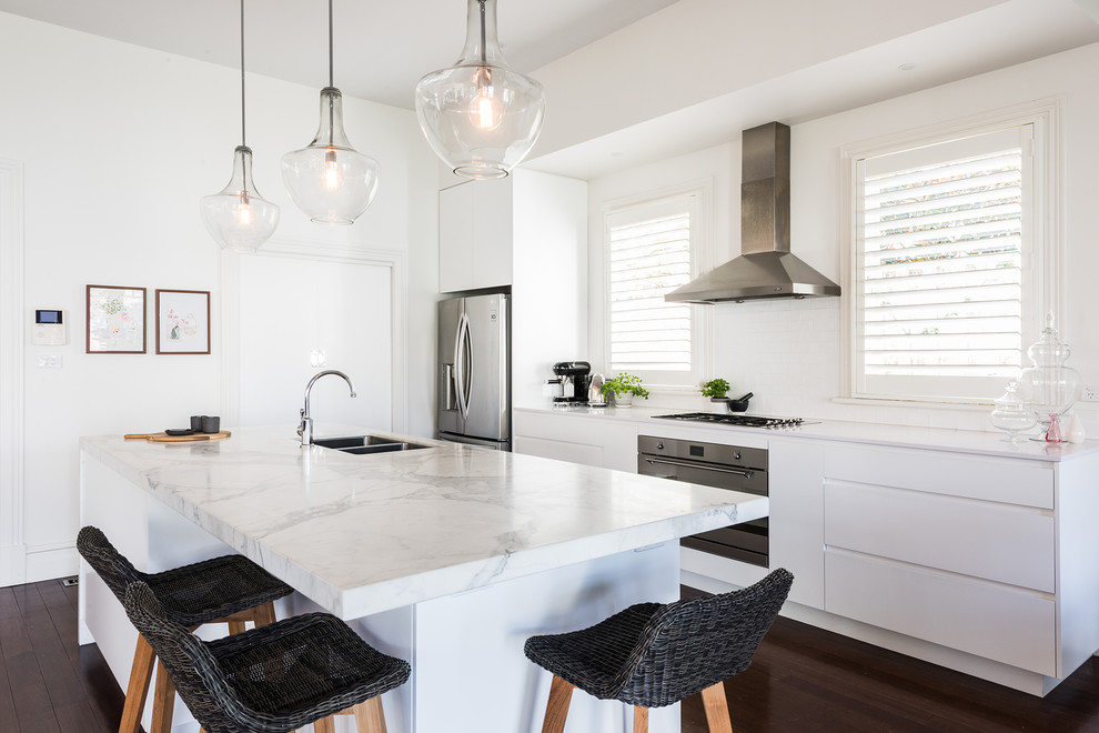 This is an example of a medium sized contemporary single-wall open plan kitchen in Melbourne with a submerged sink, flat-panel cabinets, white cabinets, marble worktops, white splashback, metro tiled splashback, stainless steel appliances, dark hardwood flooring, an island and brown floors.