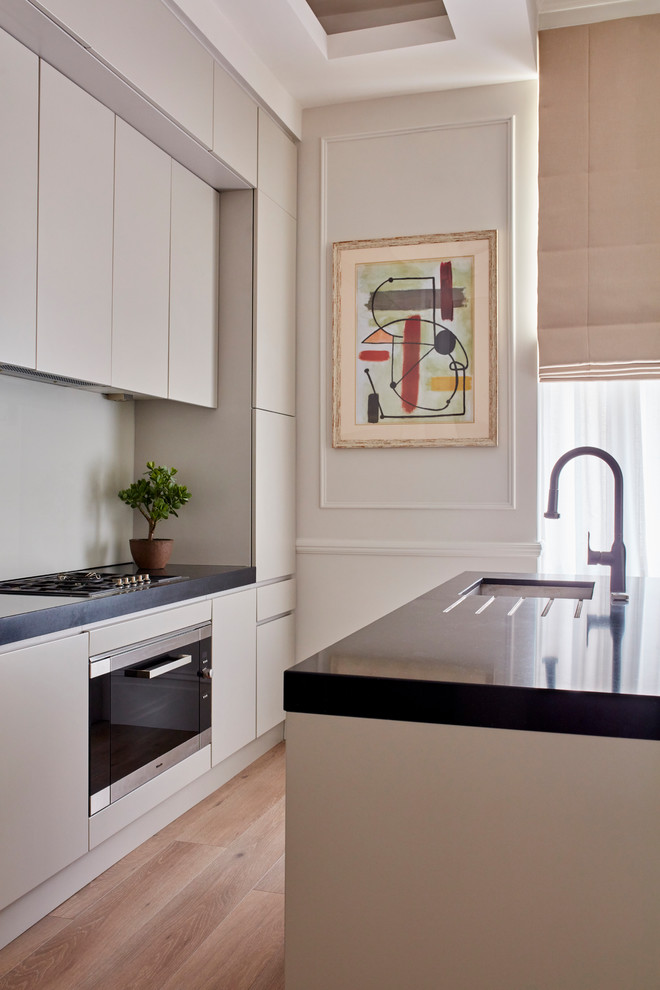This is an example of a small classic single-wall open plan kitchen in London with a submerged sink, flat-panel cabinets, beige cabinets, granite worktops, beige splashback, glass sheet splashback, integrated appliances, laminate floors, an island, beige floors and black worktops.