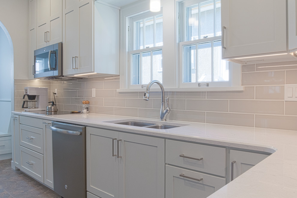 Modern inredning av ett avskilt, litet l-kök, med en dubbel diskho, vita skåp, bänkskiva i kvarts, grått stänkskydd, stänkskydd i tunnelbanekakel, rostfria vitvaror och flerfärgat golv