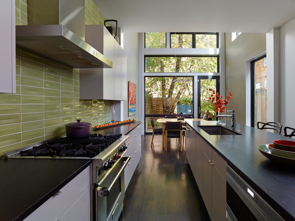 This is an example of a contemporary galley kitchen/diner in Philadelphia with a single-bowl sink, green splashback, stainless steel appliances, an island, white cabinets, glass tiled splashback and dark hardwood flooring.