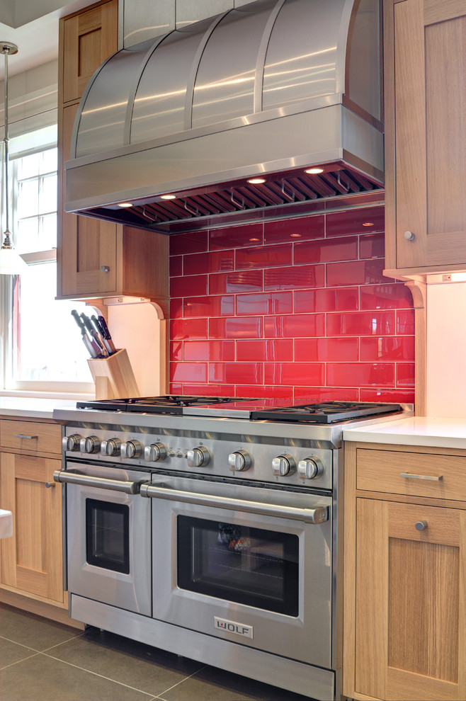 Cette photo montre une cuisine chic en bois clair avec une crédence rouge, un électroménager en acier inoxydable et une crédence en carrelage métro.