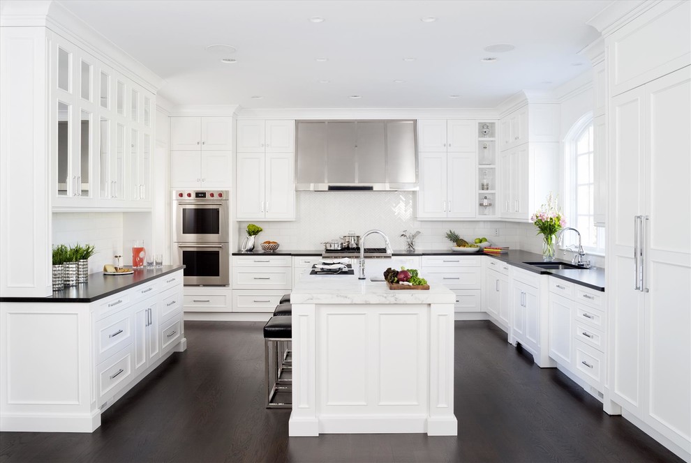 Cette image montre une cuisine traditionnelle en U avec des portes de placard blanches, une crédence blanche, parquet foncé et un sol marron.