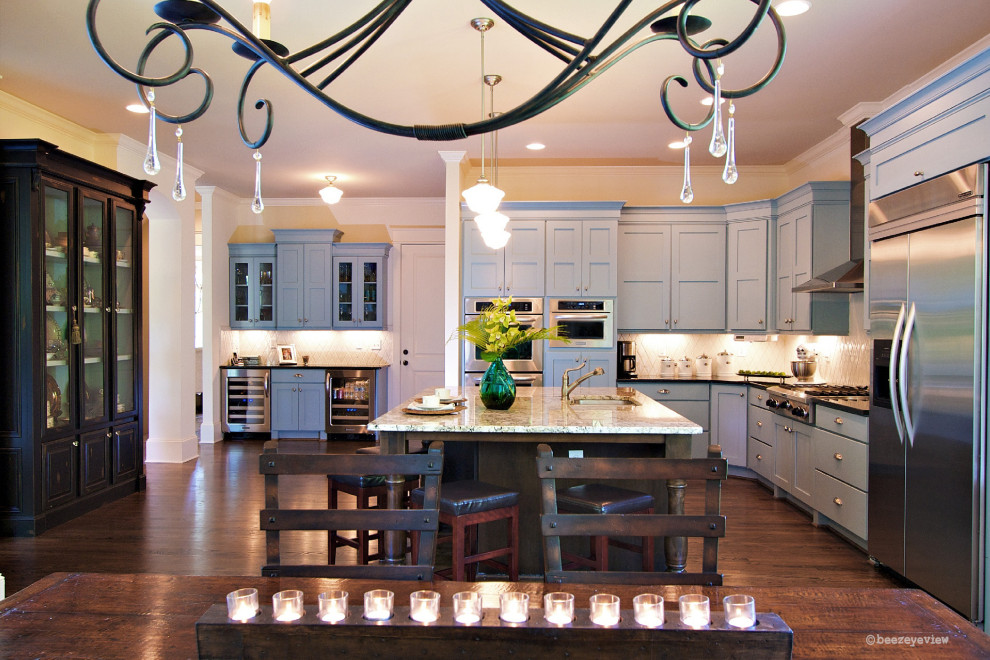 Foto på ett amerikanskt kök, med en undermonterad diskho, luckor med infälld panel, blå skåp, granitbänkskiva, beige stänkskydd, stänkskydd i cementkakel, rostfria vitvaror, mellanmörkt trägolv och en köksö