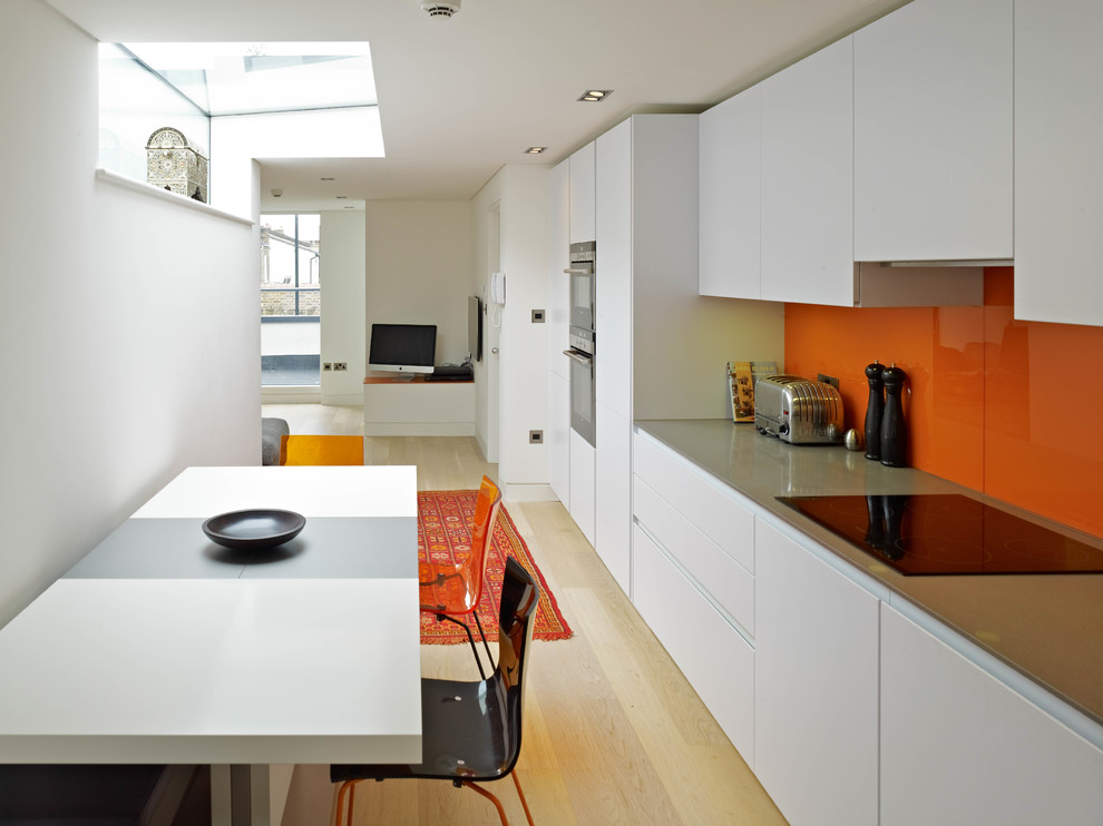 Einzeilige, Kleine Moderne Wohnküche ohne Insel mit flächenbündigen Schrankfronten, weißen Schränken, Küchenrückwand in Orange, Glasrückwand, Küchengeräten aus Edelstahl und braunem Holzboden in London