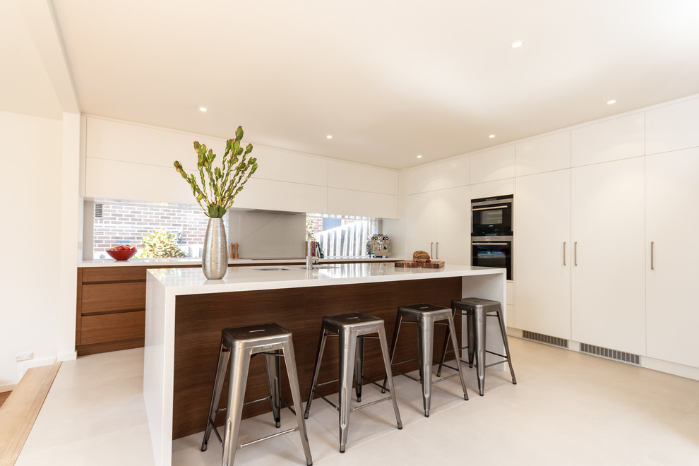 Moderne Küche in L-Form mit flächenbündigen Schrankfronten, weißen Schränken, Quarzwerkstein-Arbeitsplatte, Küchenrückwand in Grau, Glasrückwand und Kücheninsel in Melbourne