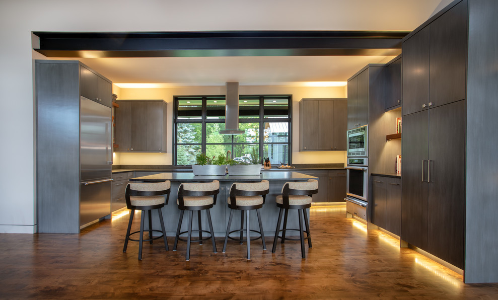 Photo of an expansive modern u-shaped kitchen/diner in Other with a submerged sink, flat-panel cabinets, grey cabinets, granite worktops, stainless steel appliances, medium hardwood flooring, an island, brown floors and black worktops.