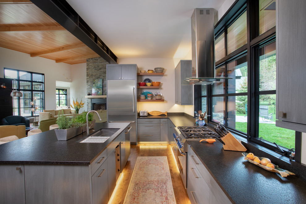 Expansive modern u-shaped kitchen/diner in Other with a submerged sink, flat-panel cabinets, grey cabinets, granite worktops, stainless steel appliances, medium hardwood flooring, an island, brown floors and black worktops.