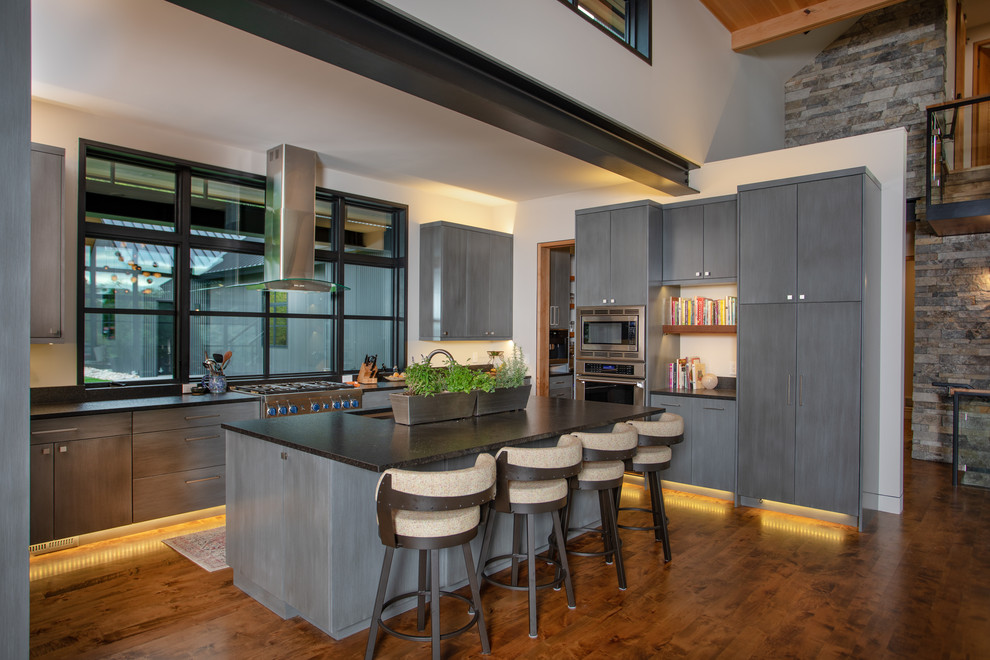 Photo of an expansive modern u-shaped kitchen/diner in Other with a submerged sink, flat-panel cabinets, grey cabinets, granite worktops, stainless steel appliances, medium hardwood flooring, an island, brown floors and black worktops.