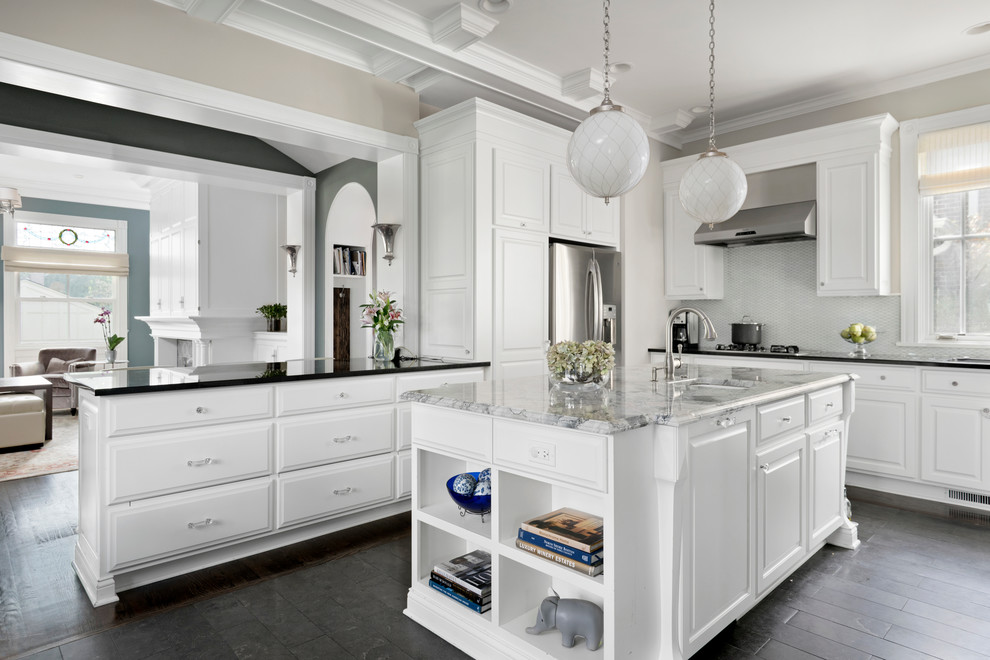 Example of a classic kitchen design in Chicago with an undermount sink, raised-panel cabinets, white backsplash, stainless steel appliances and an island