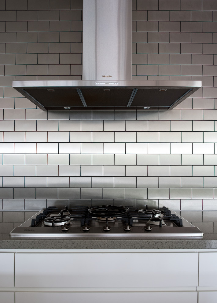 Exempel på ett stort modernt linjärt kök och matrum, med vita skåp, grått stänkskydd, stänkskydd i metallkakel, rostfria vitvaror, mellanmörkt trägolv och en köksö