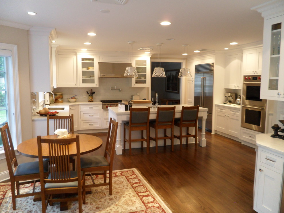 Example of a large transitional u-shaped medium tone wood floor enclosed kitchen design in New York with a single-bowl sink, shaker cabinets, white cabinets, marble countertops, gray backsplash, glass tile backsplash, stainless steel appliances and an island