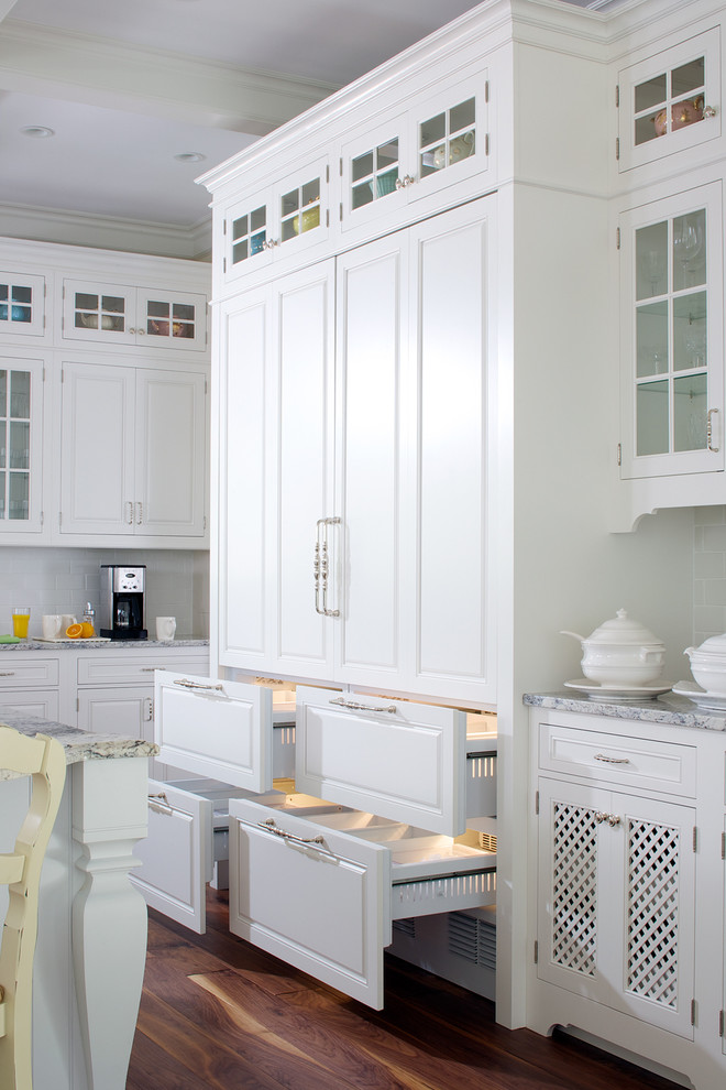 Design ideas for a traditional kitchen in Grand Rapids with raised-panel cabinets, white cabinets, white splashback, metro tiled splashback, dark hardwood flooring and an island.