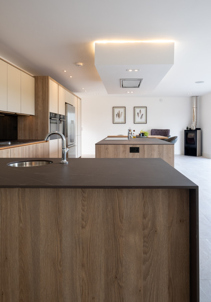 Photo of a large contemporary l-shaped open plan kitchen in Hampshire with flat-panel cabinets, white cabinets, grey splashback, glass sheet splashback, porcelain flooring, an island, multi-coloured floors and grey worktops.