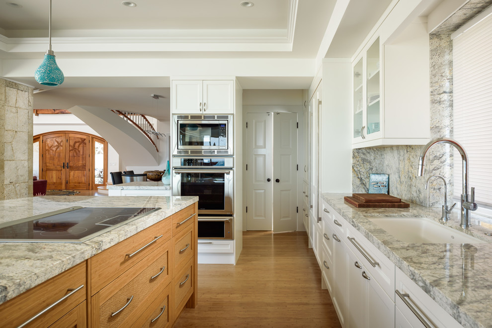 Beach style bamboo floor and brown floor kitchen photo in Hawaii with a single-bowl sink, shaker cabinets, white cabinets, granite countertops, gray backsplash, stone slab backsplash, paneled appliances and an island