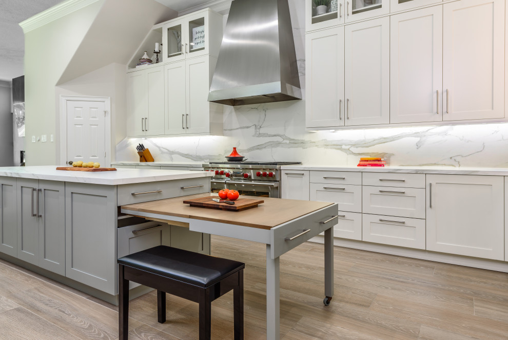 Foto på ett stort vintage vit kök, med en undermonterad diskho, skåp i shakerstil, vita skåp, marmorbänkskiva, vitt stänkskydd, stänkskydd i marmor, rostfria vitvaror, ljust trägolv, brunt golv och en köksö