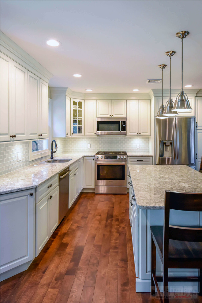 Foto på ett mellanstort kök, med en undermonterad diskho, luckor med upphöjd panel, vita skåp, bänkskiva i kvarts, grått stänkskydd, stänkskydd i glaskakel, rostfria vitvaror, plywoodgolv, en köksö och brunt golv