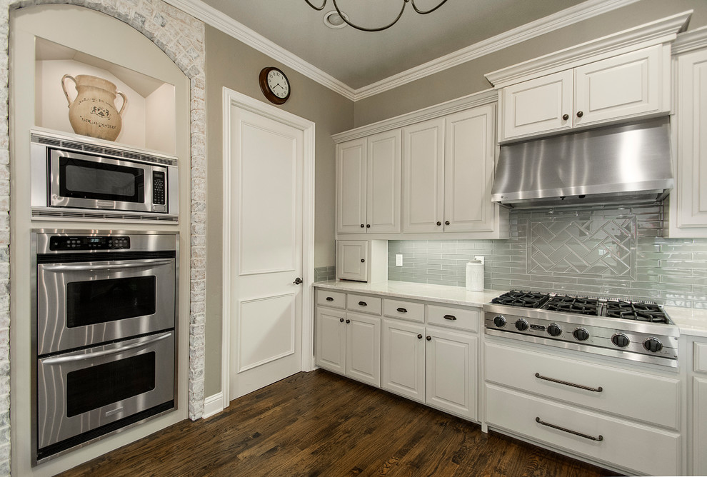 Example of a mid-sized classic l-shaped medium tone wood floor eat-in kitchen design in Dallas with an undermount sink, raised-panel cabinets, white cabinets, blue backsplash, glass tile backsplash, stainless steel appliances, a peninsula and granite countertops