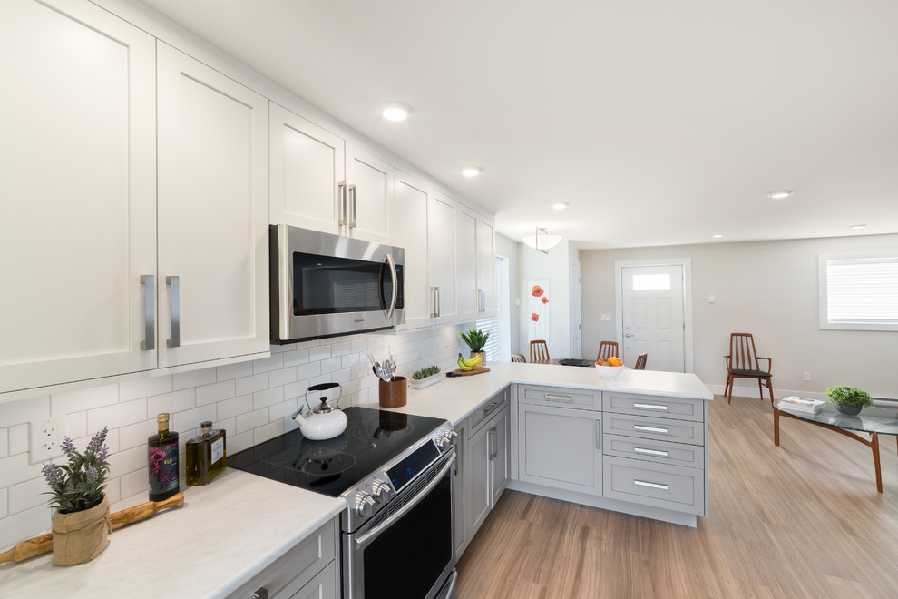 Example of a mid-sized transitional galley vinyl floor eat-in kitchen design in Vancouver with a drop-in sink, shaker cabinets, gray cabinets, laminate countertops, white backsplash, subway tile backsplash, stainless steel appliances and a peninsula