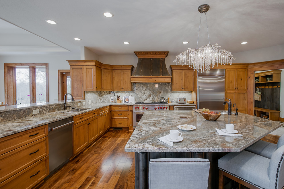 This is an example of a large rustic u-shaped kitchen/diner in Cleveland with a double-bowl sink, recessed-panel cabinets, medium wood cabinets, engineered stone countertops, grey splashback, porcelain splashback, stainless steel appliances, medium hardwood flooring, an island and grey worktops.