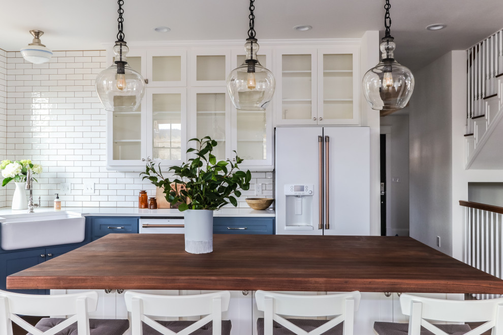 Example of a large cottage u-shaped medium tone wood floor and brown floor eat-in kitchen design in Seattle with a farmhouse sink, shaker cabinets, blue cabinets, quartz countertops, white backsplash, subway tile backsplash, white appliances, an island and white countertops