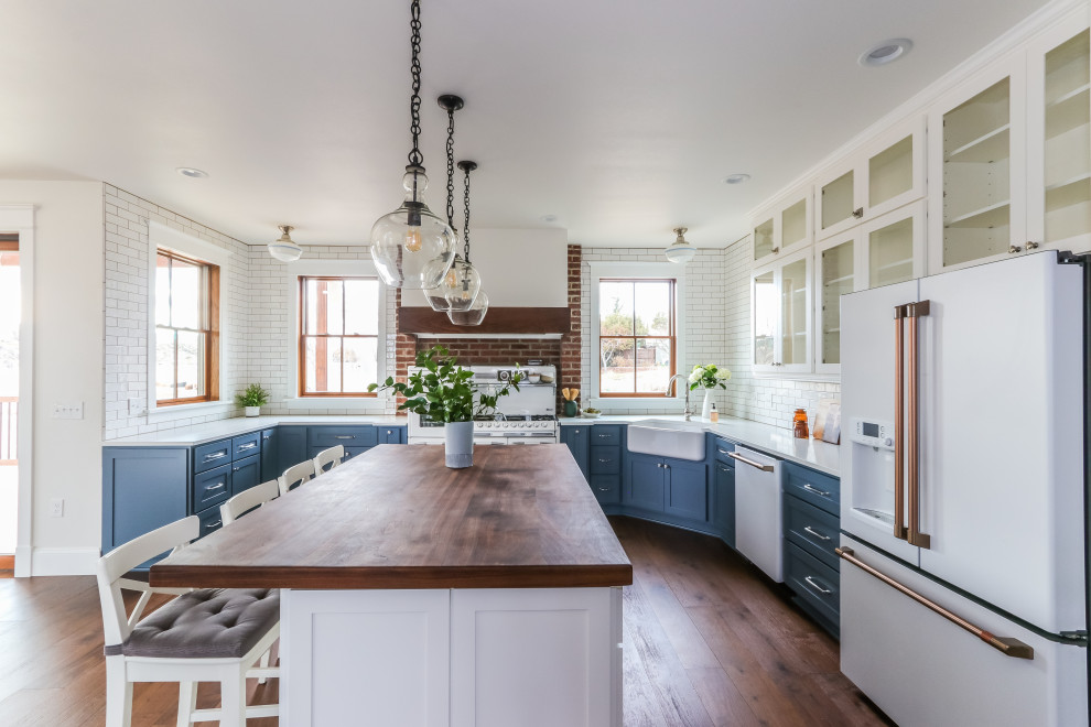 Inspiration for a large cottage u-shaped medium tone wood floor and brown floor eat-in kitchen remodel in Seattle with a farmhouse sink, shaker cabinets, blue cabinets, quartz countertops, white backsplash, subway tile backsplash, white appliances, an island and white countertops