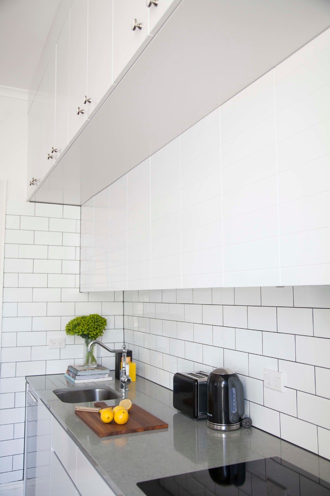 Immagine di una cucina minimal di medie dimensioni con ante bianche, top in marmo, paraspruzzi nero e elettrodomestici neri