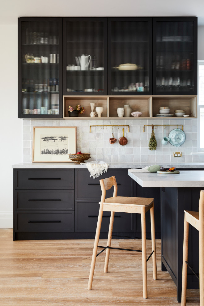 This is an example of a medium sized midcentury l-shaped kitchen/diner in Sydney with a belfast sink, shaker cabinets, black cabinets, marble worktops, grey splashback, ceramic splashback, stainless steel appliances, light hardwood flooring, an island, brown floors and grey worktops.