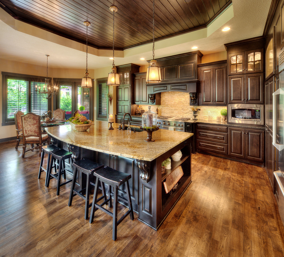 Large tuscan l-shaped kitchen photo in Kansas City with an undermount sink, raised-panel cabinets, dark wood cabinets, granite countertops, beige backsplash, stainless steel appliances and an island