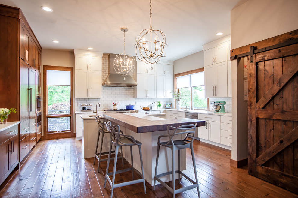 Inspiration for a huge transitional l-shaped medium tone wood floor kitchen pantry remodel in St Louis with an undermount sink, shaker cabinets, white cabinets, wood countertops, white backsplash, subway tile backsplash, stainless steel appliances and an island