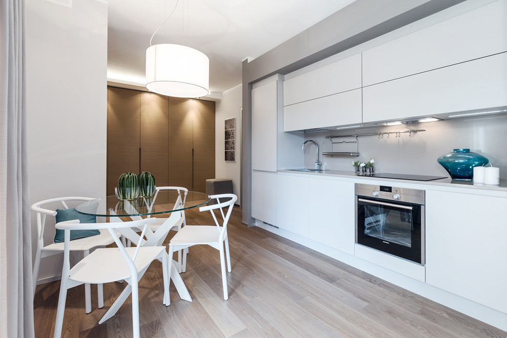 Einzeilige Moderne Wohnküche mit flächenbündigen Schrankfronten, weißen Schränken, Küchenrückwand in Grau, Küchengeräten aus Edelstahl und hellem Holzboden in Sonstige