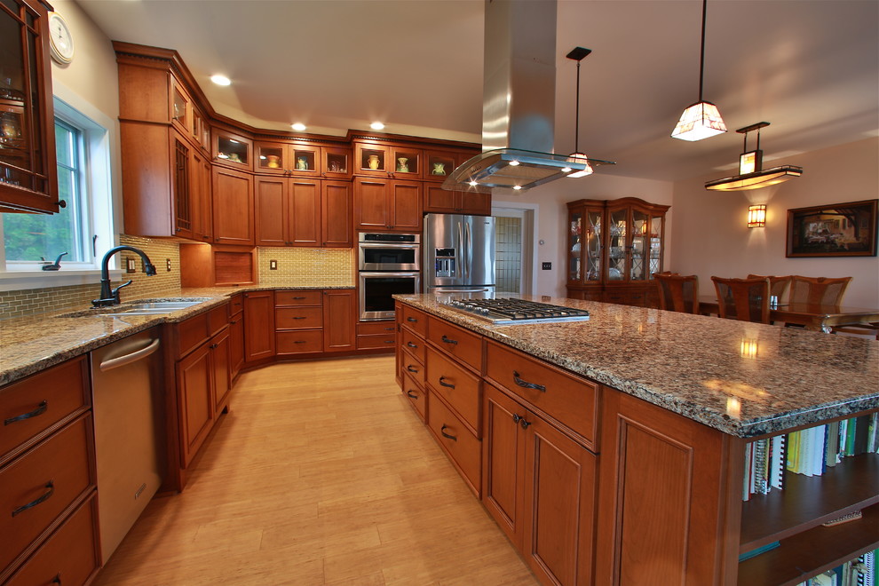 This is an example of a large traditional l-shaped kitchen/diner in Burlington with a triple-bowl sink, flat-panel cabinets, medium wood cabinets, engineered stone countertops, green splashback, glass tiled splashback, stainless steel appliances, bamboo flooring and an island.