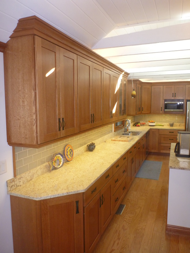 Example of a small classic galley light wood floor enclosed kitchen design in Boston with an undermount sink, recessed-panel cabinets, medium tone wood cabinets, granite countertops, beige backsplash, subway tile backsplash and stainless steel appliances