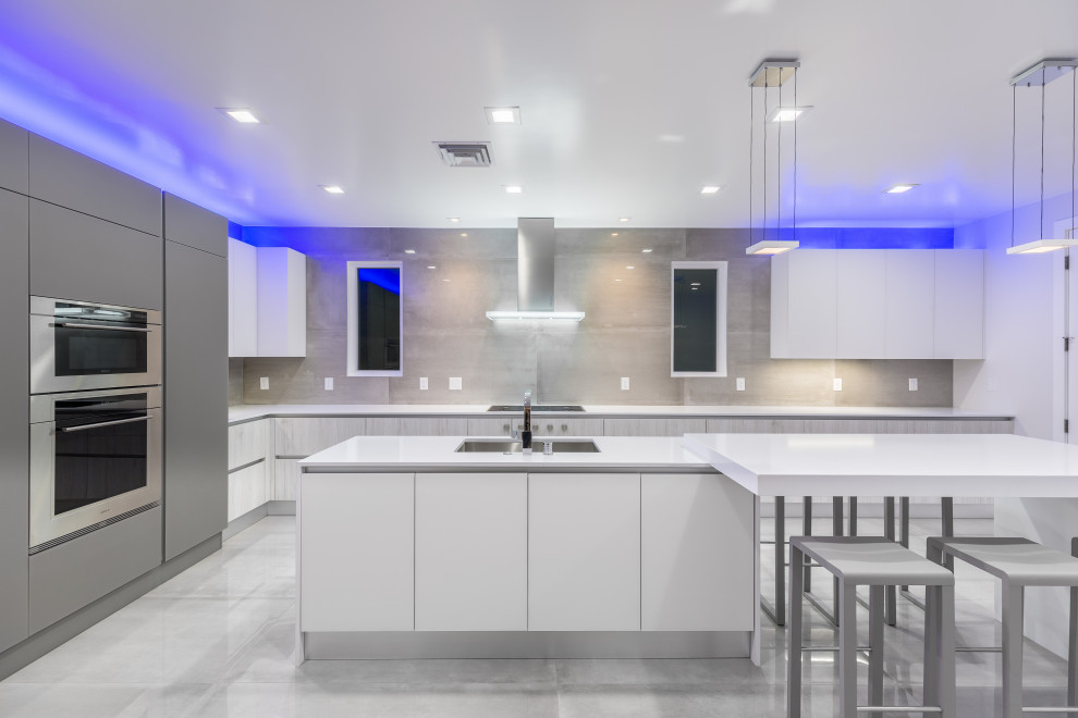 This is an example of a medium sized modern l-shaped enclosed kitchen in Las Vegas with a submerged sink, flat-panel cabinets, white cabinets, engineered stone countertops, beige splashback, porcelain splashback, stainless steel appliances, porcelain flooring, an island, grey floors and white worktops.