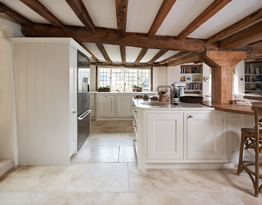 This is an example of a medium sized farmhouse kitchen/diner in Oxfordshire with composite countertops, stainless steel appliances, limestone flooring, an island, beige floors, a submerged sink, recessed-panel cabinets and white cabinets.