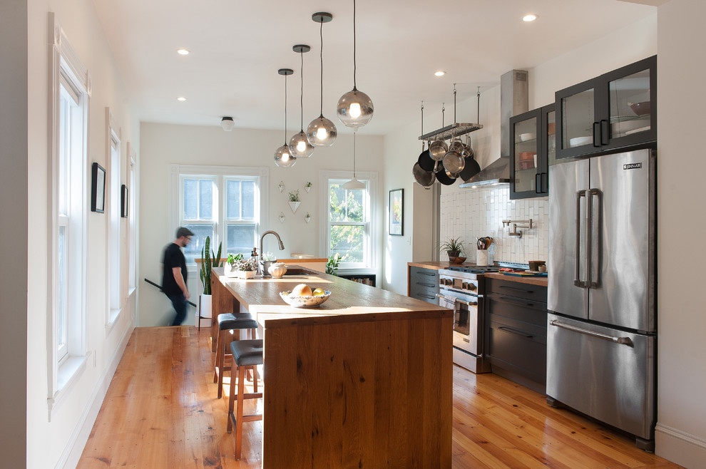 This is an example of a traditional kitchen in Boston with glass-front cabinets, black cabinets, wood worktops, white splashback, stainless steel appliances, medium hardwood flooring and an island.