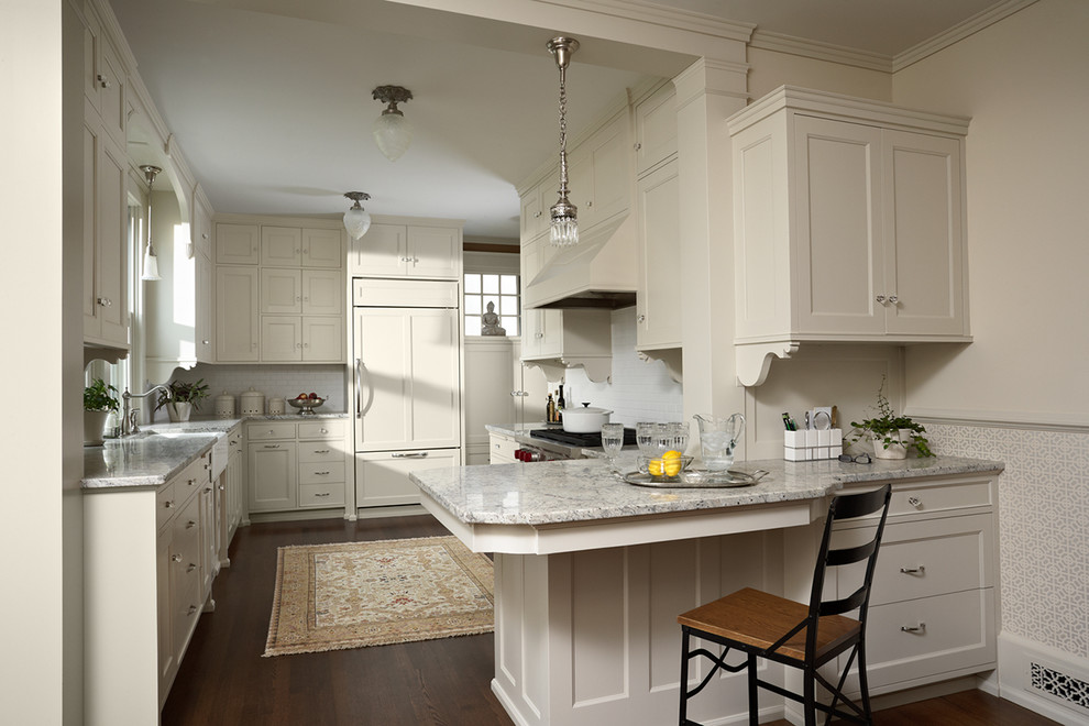 Mid-sized ornate u-shaped dark wood floor and brown floor eat-in kitchen photo in Minneapolis with a farmhouse sink, recessed-panel cabinets, white cabinets, granite countertops, white backsplash, ceramic backsplash, paneled appliances and a peninsula