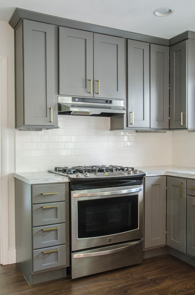Exempel på ett mellanstort 60 tals kök, med en rustik diskho, skåp i shakerstil, grå skåp, laminatbänkskiva, vitt stänkskydd, stänkskydd i tunnelbanekakel, rostfria vitvaror, mellanmörkt trägolv och en halv köksö