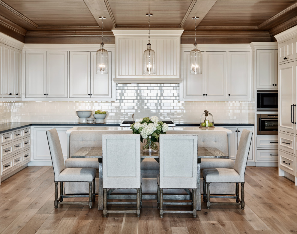 Inspiration for a timeless u-shaped medium tone wood floor, brown floor and wood ceiling eat-in kitchen remodel in Phoenix with an undermount sink, recessed-panel cabinets, white cabinets, white backsplash, subway tile backsplash, paneled appliances, an island and black countertops