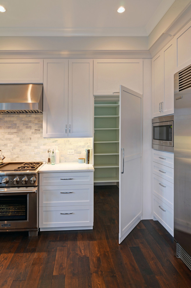 Exempel på ett stort klassiskt kök, med en undermonterad diskho, skåp i shakerstil, vita skåp, bänkskiva i kvarts, vitt stänkskydd, stänkskydd i stenkakel, rostfria vitvaror, mellanmörkt trägolv och en köksö