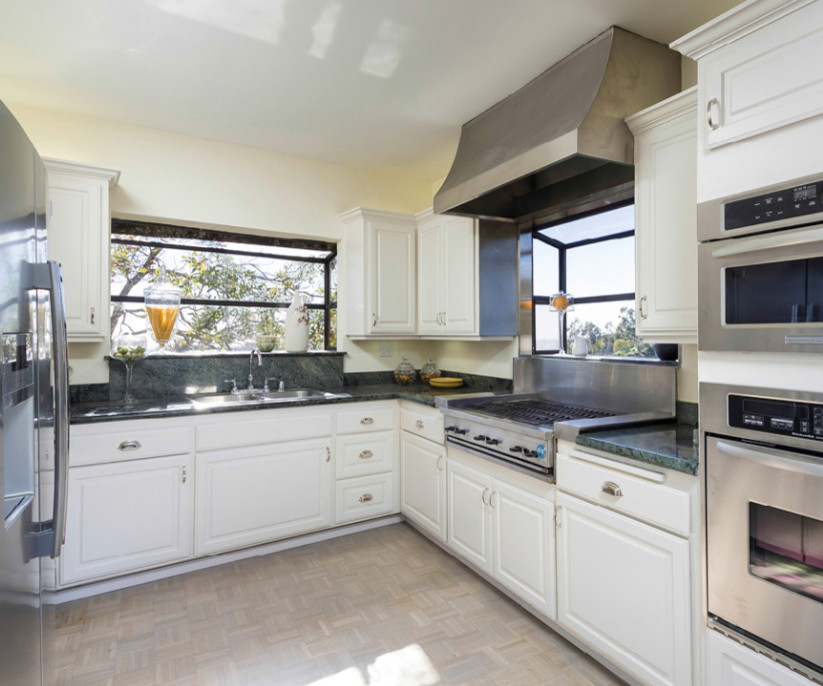 This is an example of a medium sized classic u-shaped open plan kitchen in Los Angeles with a built-in sink, raised-panel cabinets, white cabinets, engineered stone countertops, grey splashback, stone slab splashback, stainless steel appliances, vinyl flooring, no island and grey floors.