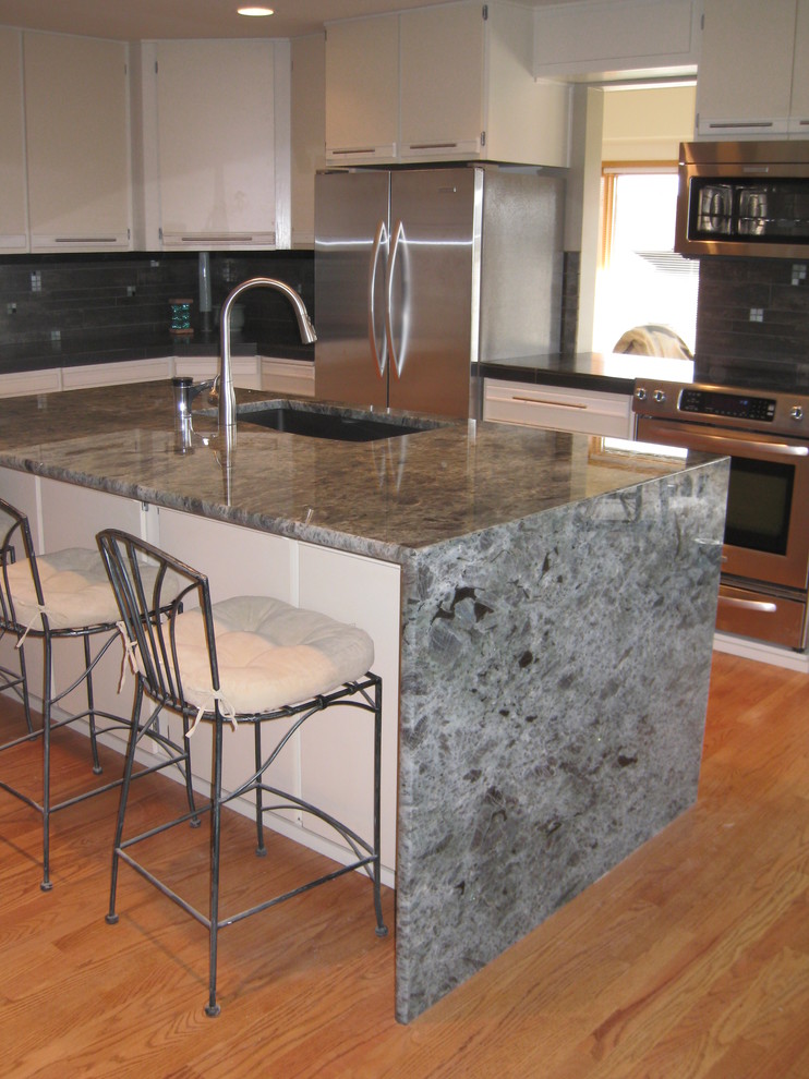 Example of a mid-sized transitional u-shaped light wood floor eat-in kitchen design in Seattle with an undermount sink, flat-panel cabinets, white cabinets, quartzite countertops, metallic backsplash, porcelain backsplash, stainless steel appliances and an island