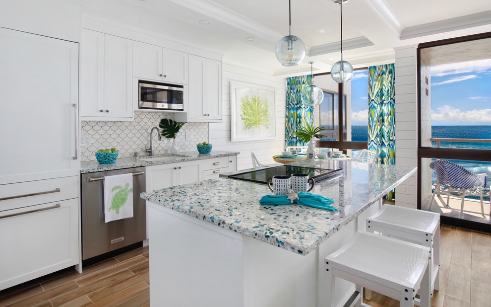 Photo of a beach style galley open plan kitchen in Hawaii with a submerged sink, shaker cabinets, white cabinets, white splashback, integrated appliances, medium hardwood flooring, an island, brown floors and multicoloured worktops.