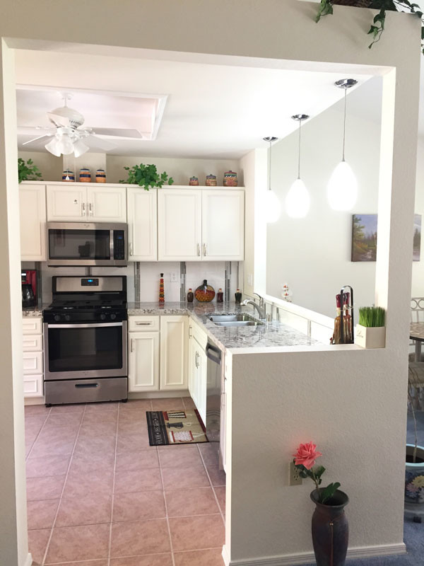 Small classic l-shaped kitchen pantry in Las Vegas with a double-bowl sink, beaded cabinets, white cabinets, engineered stone countertops, white splashback, porcelain splashback, stainless steel appliances, porcelain flooring, no island and pink floors.