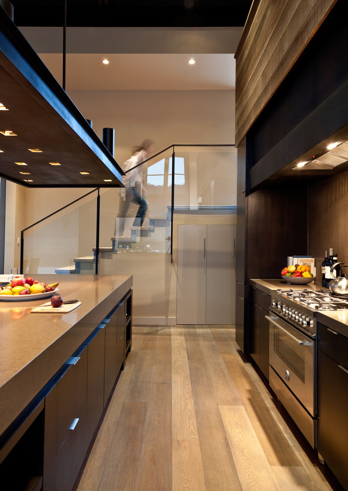 Cette image montre une cuisine design avec un placard à porte plane, des portes de placard marrons, une crédence marron et un électroménager en acier inoxydable.
